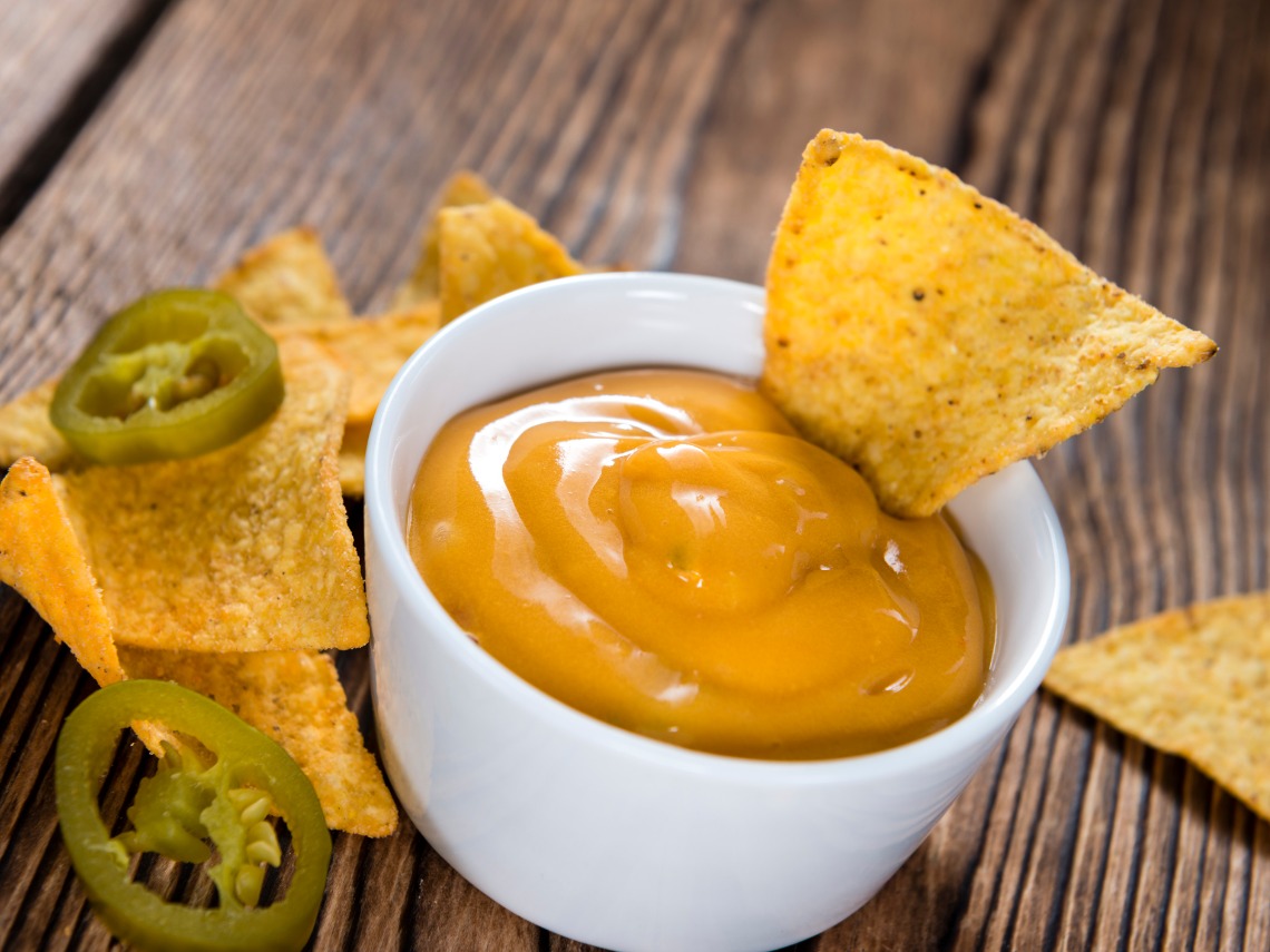 salsa cheddar en cuenco blanco junto a plato de nachos