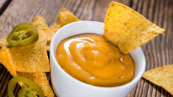 salsa cheddar en cuenco blanco junto a plato de nachos