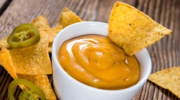 salsa cheddar en cuenco blanco junto a plato de nachos