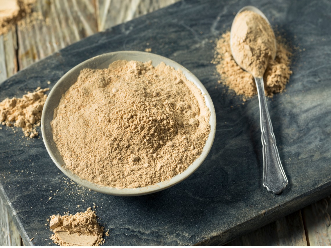 maca en polvo en cuenco blanco y cuchara sobre mesa negra