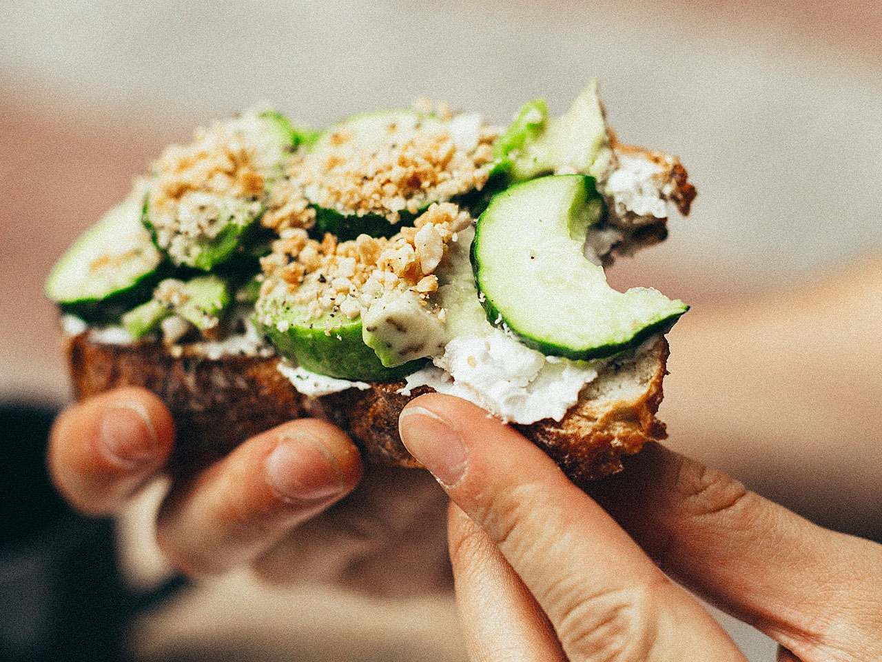 manos sujetando una tosta integral de pepino y queso