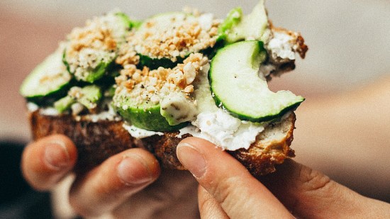manos sujetando una tosta integral de pepino y queso