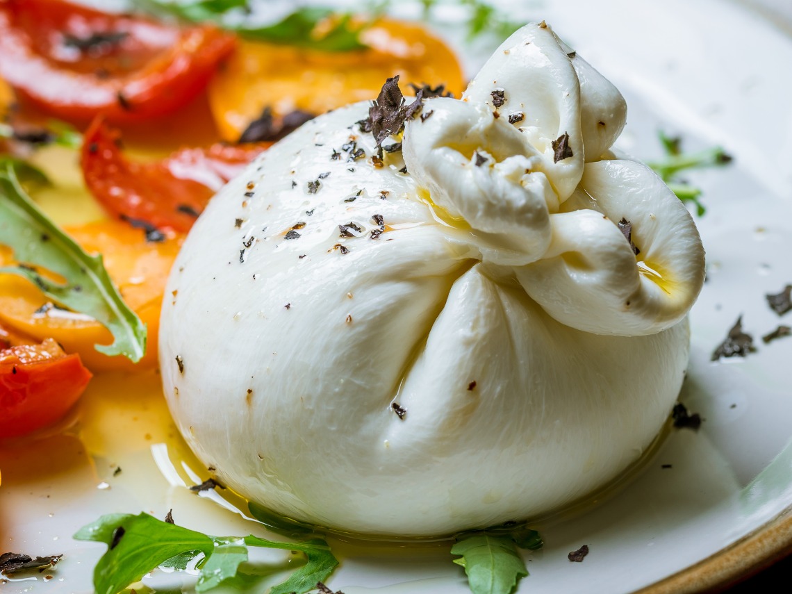 burrata con tomate y albahaca sobre plato blanco primer plano