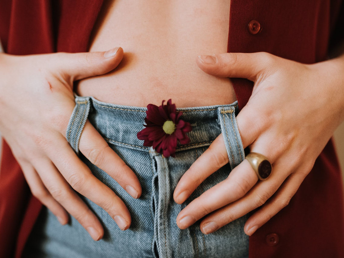 abdomen de mujer con vaqueros y manos en los bolsillos con flor roja en el boton