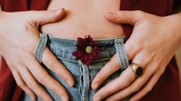 abdomen de mujer con vaqueros y manos en los bolsillos con flor roja en el boton