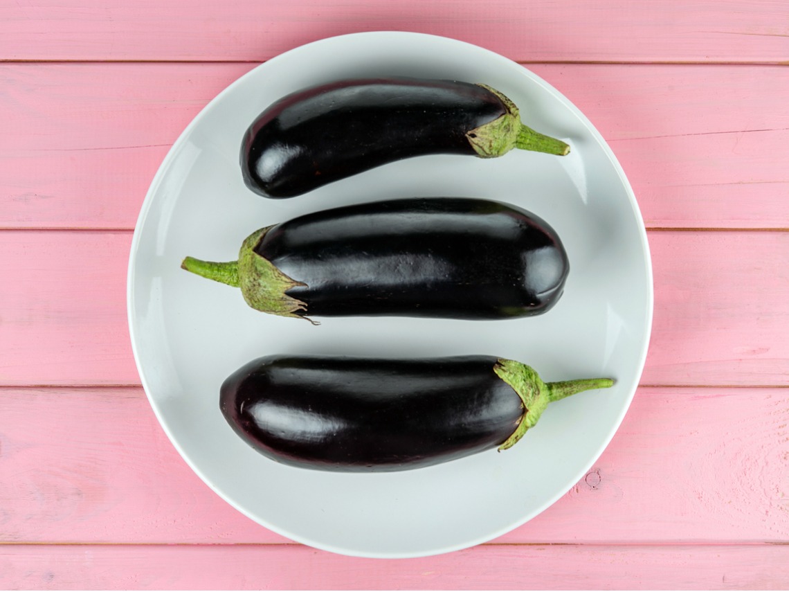 plano zenital berenjenas sobre plato blanco en mesa de madera rosa