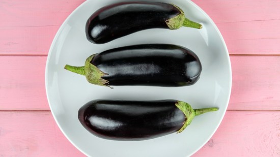 plano zenital berenjenas sobre plato blanco en mesa de madera rosa