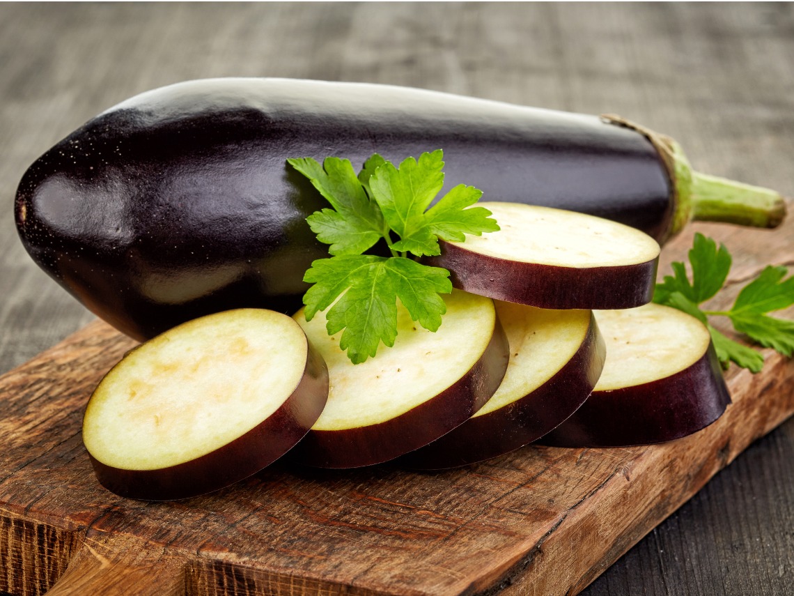 berenjena y rodajas de berenjena sobre tabla de madera en mesa de madera