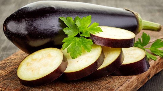 berenjena y rodajas de berenjena sobre tabla de madera en mesa de madera