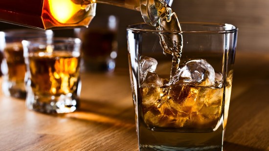 coctelera vertiendo whisky en vaso sobre mesa de madera