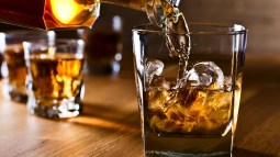 coctelera vertiendo whisky en vaso sobre mesa de madera