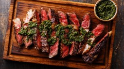 plano zenital carne troceada a la parrilla sobre mesa de madera y salsa chimichurri
