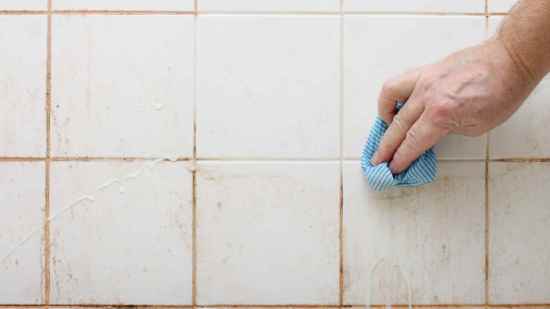 Mano limpiando juntas negras de los azulejos del baño con paño y truco casero sin productos químicos