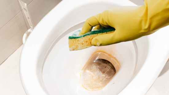 Mano con guante limpiando el sarro del inodoro con esponja y vinagre